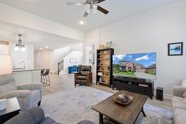 living room with ceiling fan with notable chandelier, light hardwood / wood-style flooring, and sink