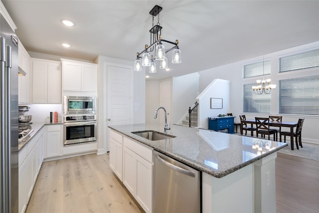 kitchen featuring white cabinets, hanging light fixtures, stainless steel appliances, and a kitchen island with sink