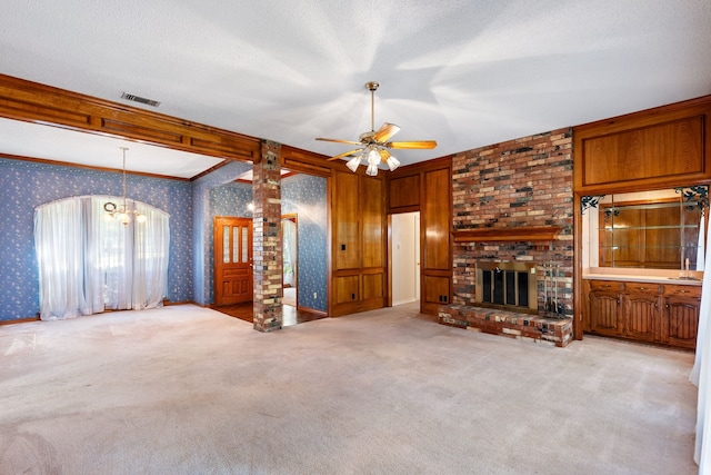 unfurnished living room featuring ceiling fan with notable chandelier, a textured ceiling, a fireplace, and light colored carpet