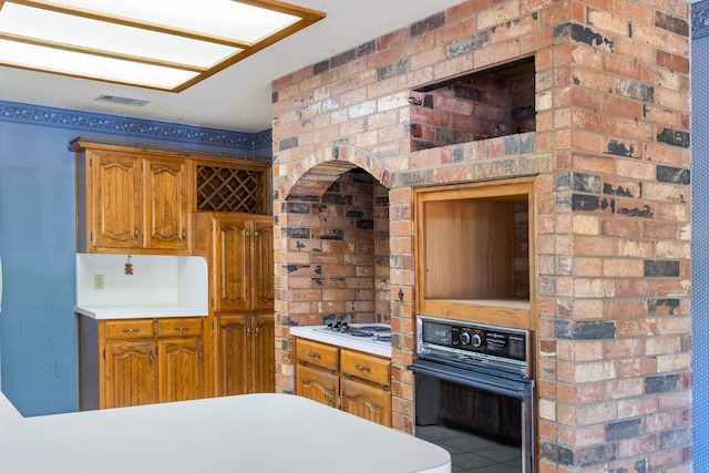 kitchen featuring brick wall, white gas cooktop, oven, and light tile patterned flooring