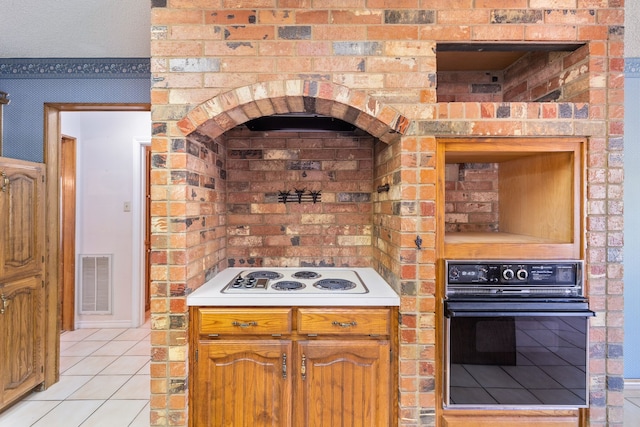 kitchen with white electric cooktop, brick wall, light tile patterned flooring, and black oven