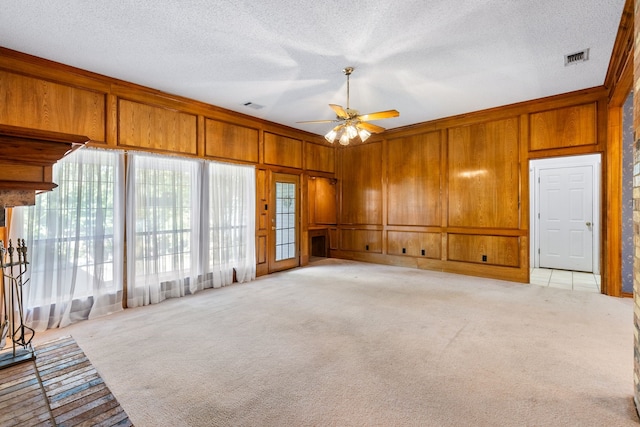 unfurnished living room featuring light colored carpet, a textured ceiling, wood walls, and ceiling fan