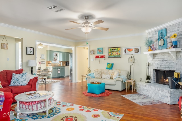 living room featuring crown molding, ceiling fan, a brick fireplace, and hardwood / wood-style flooring