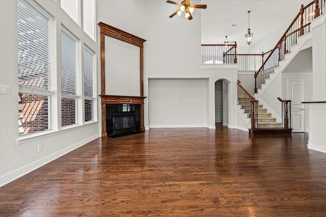 unfurnished living room with a tiled fireplace, dark hardwood / wood-style flooring, a towering ceiling, and ceiling fan with notable chandelier