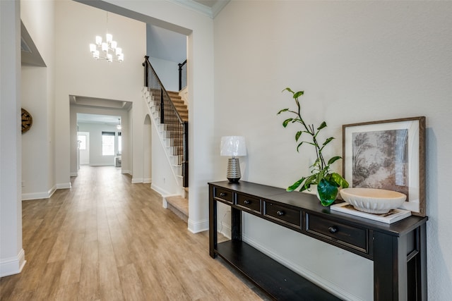 foyer featuring light hardwood / wood-style floors, ornamental molding, a towering ceiling, and a chandelier