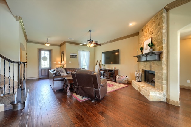 living room with ceiling fan, dark wood-type flooring, crown molding, and a stone fireplace