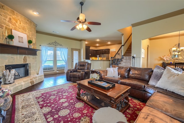 living room featuring dark hardwood / wood-style floors, ceiling fan with notable chandelier, crown molding, and a stone fireplace