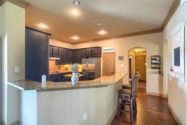 kitchen featuring light stone countertops, dark brown cabinetry, dark hardwood / wood-style flooring, stainless steel fridge, and kitchen peninsula