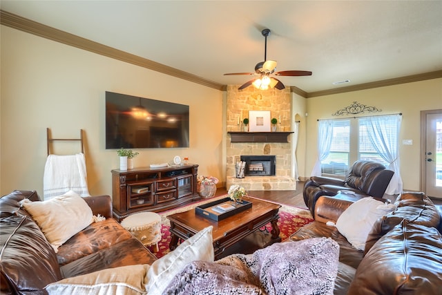 living room with ceiling fan, ornamental molding, hardwood / wood-style flooring, and a stone fireplace