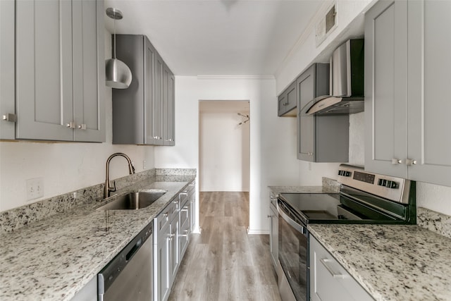 kitchen featuring light wood-type flooring, stainless steel appliances, sink, wall chimney exhaust hood, and pendant lighting