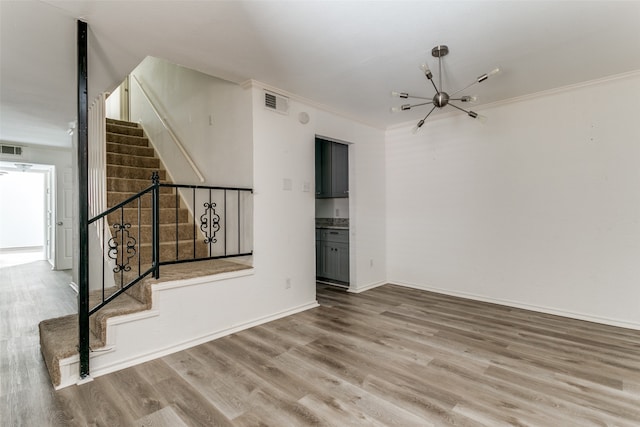 spare room featuring ornamental molding, wood-type flooring, and an inviting chandelier