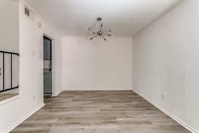 empty room with crown molding, a chandelier, and light hardwood / wood-style floors