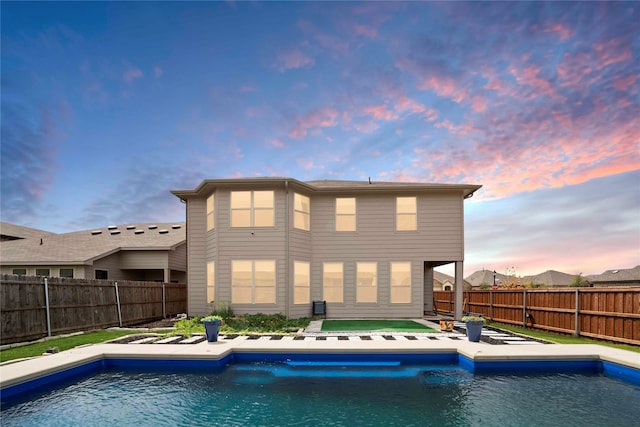 back house at dusk featuring a fenced in pool