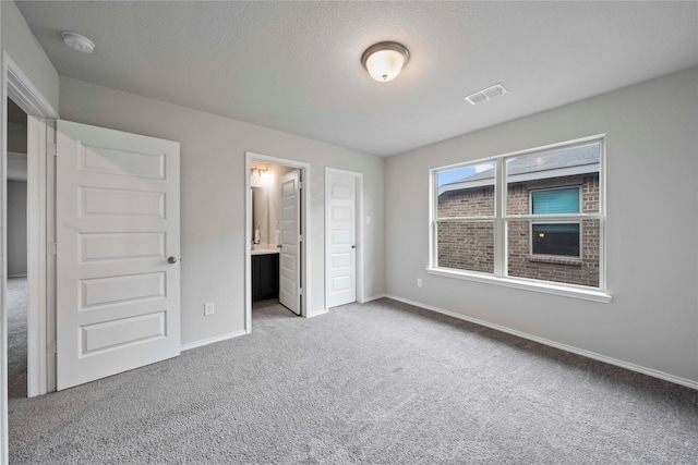 unfurnished bedroom featuring connected bathroom, a textured ceiling, and light colored carpet