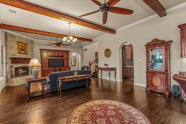 living room with beamed ceiling, crown molding, dark wood-type flooring, a stone fireplace, and ceiling fan with notable chandelier