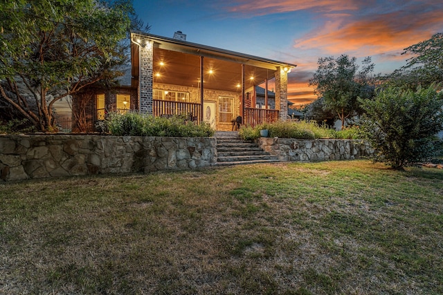 back house at dusk with a porch and a yard