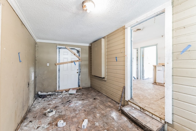 interior space with ornamental molding, a textured ceiling, and wood walls