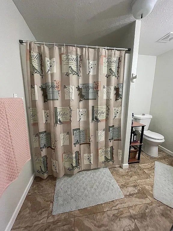 bathroom with vaulted ceiling, toilet, a shower with shower curtain, and a textured ceiling