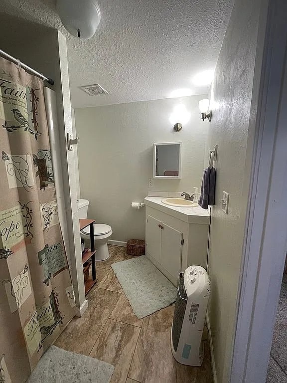 bathroom with curtained shower, toilet, a textured ceiling, and vanity