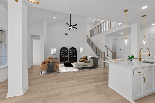 kitchen featuring sink, decorative light fixtures, light wood-type flooring, an island with sink, and white cabinets