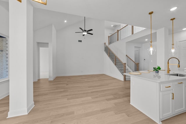 kitchen with sink, an island with sink, white cabinets, decorative light fixtures, and light wood-type flooring