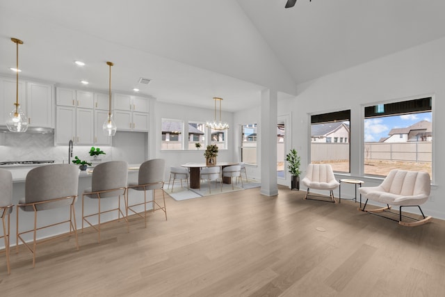 kitchen with a breakfast bar area, white cabinetry, tasteful backsplash, hanging light fixtures, and light wood-type flooring