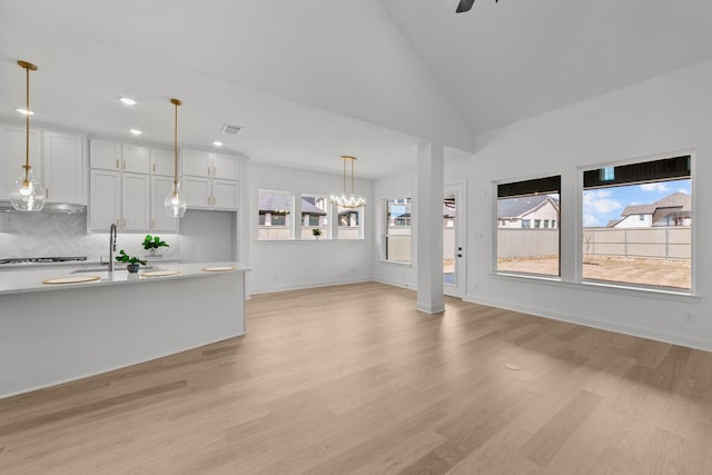 unfurnished living room with ceiling fan, high vaulted ceiling, sink, and light wood-type flooring