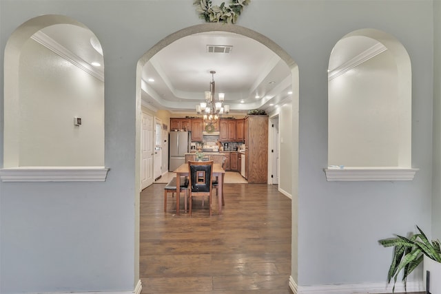 corridor with ornamental molding, a raised ceiling, a notable chandelier, and dark hardwood / wood-style floors