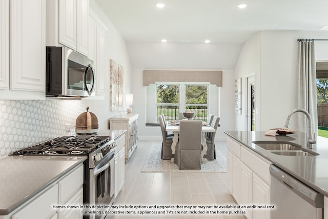 kitchen with tasteful backsplash, stainless steel appliances, sink, lofted ceiling, and white cabinets