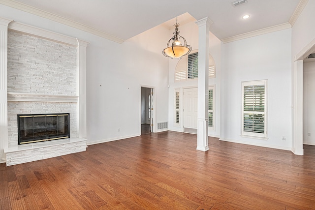 unfurnished living room featuring crown molding, hardwood / wood-style flooring, a fireplace, a towering ceiling, and ornate columns