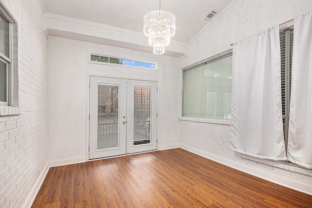 empty room with a healthy amount of sunlight, crown molding, hardwood / wood-style floors, and brick wall