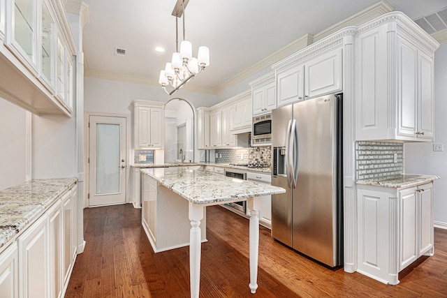 kitchen with white cabinets, hanging light fixtures, appliances with stainless steel finishes, dark hardwood / wood-style floors, and a center island