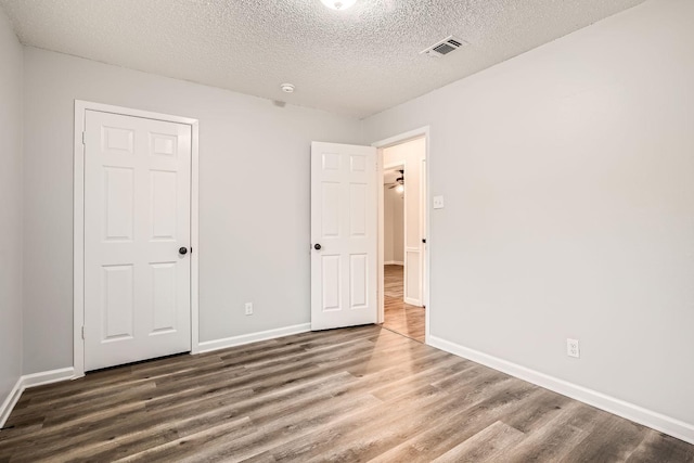 unfurnished bedroom featuring visible vents, a textured ceiling, baseboards, and wood finished floors