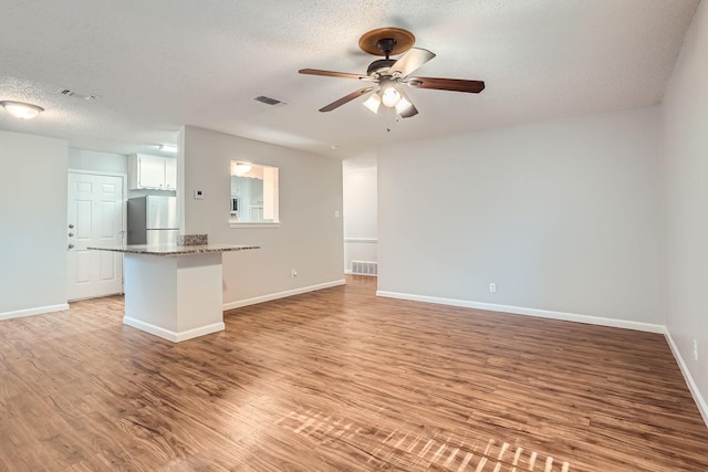 unfurnished living room with light wood finished floors, visible vents, baseboards, ceiling fan, and a textured ceiling