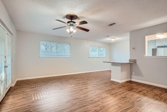 empty room featuring visible vents, a ceiling fan, a textured ceiling, wood finished floors, and baseboards