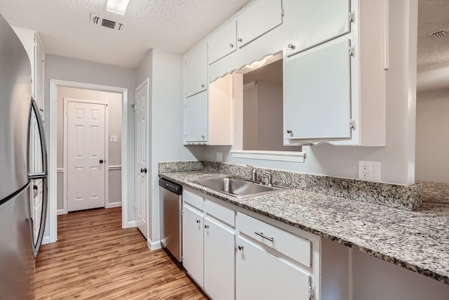 kitchen featuring a textured ceiling, light hardwood / wood-style flooring, appliances with stainless steel finishes, sink, and white cabinets