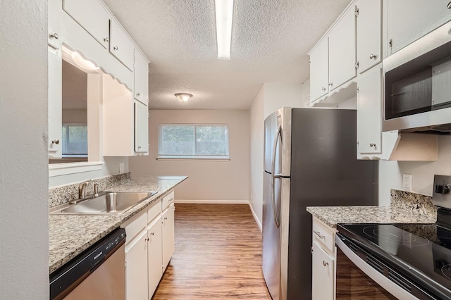 kitchen with white cabinets, stainless steel appliances, light countertops, and a sink