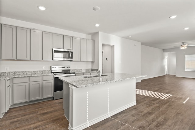 kitchen featuring dark hardwood / wood-style flooring, sink, light stone countertops, a center island with sink, and stainless steel appliances