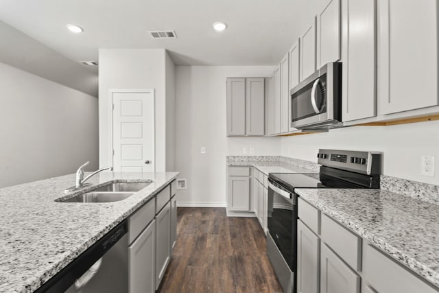 kitchen with appliances with stainless steel finishes, sink, gray cabinetry, light stone counters, and dark hardwood / wood-style floors