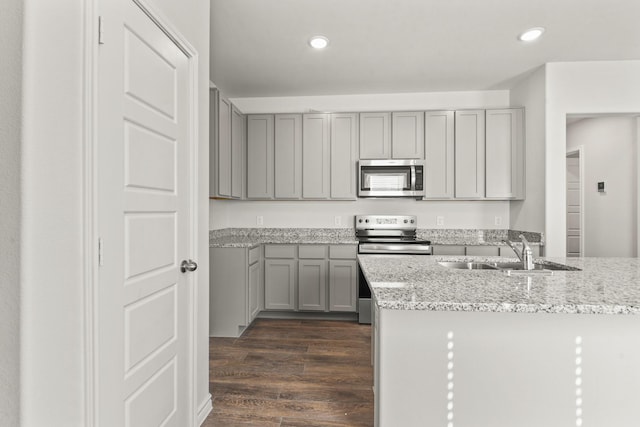 kitchen with light stone countertops, appliances with stainless steel finishes, dark wood-type flooring, sink, and gray cabinets