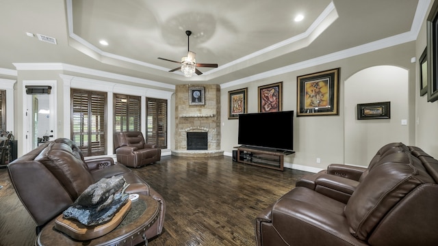 living room with dark wood-type flooring, a tray ceiling, ceiling fan, and a fireplace