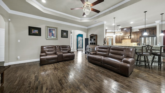 living room featuring ceiling fan with notable chandelier, a raised ceiling, dark hardwood / wood-style flooring, and crown molding