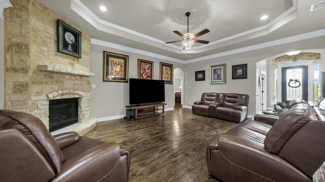 living room with dark hardwood / wood-style flooring, a fireplace, a tray ceiling, ornamental molding, and ceiling fan