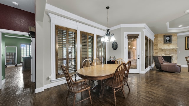 dining room with an inviting chandelier, a tray ceiling, dark hardwood / wood-style floors, a stone fireplace, and ornamental molding