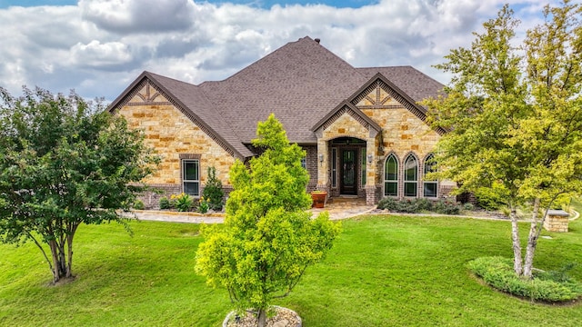 french provincial home with stone siding, roof with shingles, and a front lawn