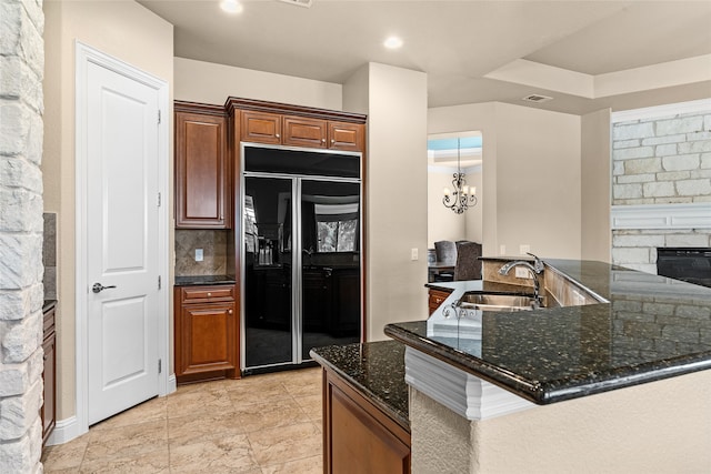 kitchen featuring black built in refrigerator, sink, dark stone countertops, a chandelier, and decorative backsplash