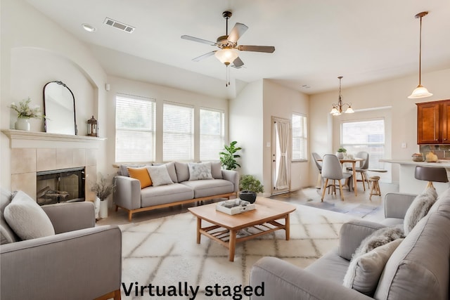 living room featuring light hardwood / wood-style flooring, a wealth of natural light, a tile fireplace, and ceiling fan with notable chandelier