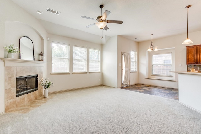 unfurnished living room featuring ceiling fan with notable chandelier, light carpet, a tile fireplace, and a healthy amount of sunlight