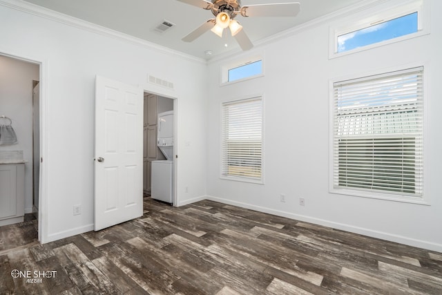 unfurnished bedroom featuring dark hardwood / wood-style flooring, ceiling fan, stacked washer / drying machine, and multiple windows