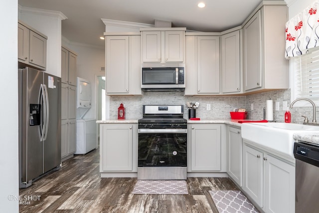 kitchen with backsplash, stacked washer / drying machine, stainless steel appliances, dark hardwood / wood-style floors, and ornamental molding